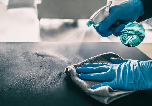 Gloved hands spraying and wiping a surface